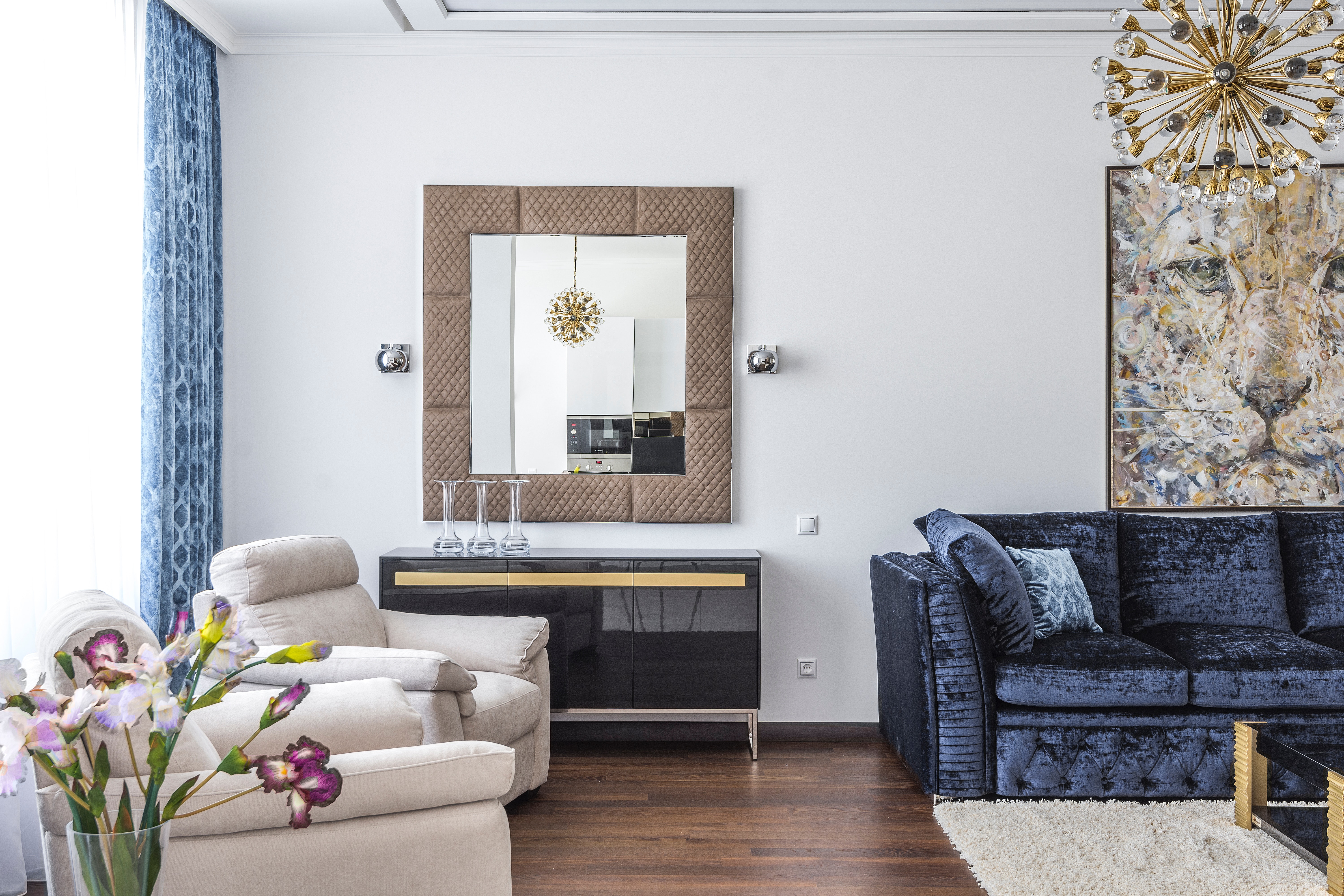 Living room, laminate flooring, mirror with wooden frame, sunlight coming through, white carpet, and art painting